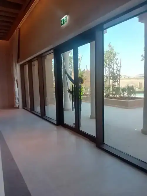 فني شركة الجواد يقوم بتلميع إطارات الألمنيوم وتنظيف الزجاج الخارجي لمبنى تجاري في الرياض بدقة عالية