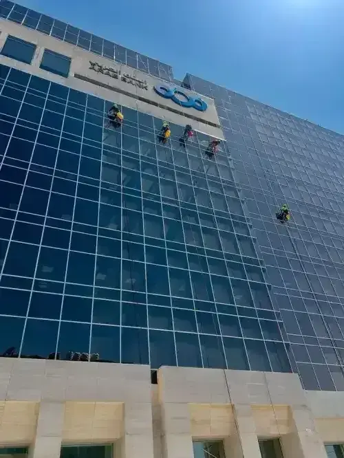 عمال أفضل شركة تنظيف واجهات زجاج بالرياض يستخدمون أدوات التلميع المتطورة لتنظيف واجهة برج إداري شاهق.