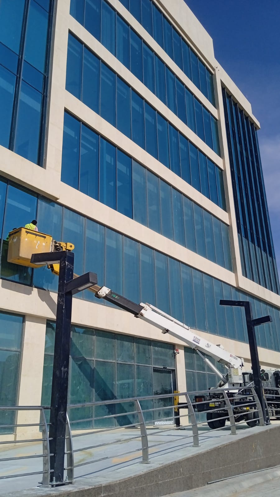 فريق شركة الجواد يقوم بتنظيف واجهة زجاجية لمقر شركة في حي غرناطة بالرياض باستخدام الرافعات الحديثة.