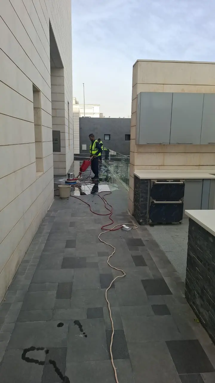 فني شركة الجواد يستخدم رافعة هيدروليكية ومسدس مياه بضغط عالي لتنظيف مسام واجهة فيلا مكسوة بكسر الرخام الأبيض والرمادي بالرياض