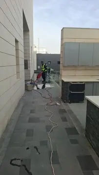 فني شركة الجواد يستخدم رافعة هيدروليكية ومسدس مياه بضغط عالي لتنظيف مسام واجهة فيلا مكسوة بكسر الرخام الأبيض والرمادي بالرياض