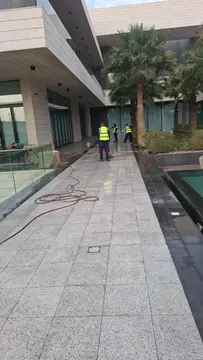 فني من شركة الجواد يستخدم مضخة مياه فائقة الضغط وغسالة اللباد لجلي وتنظيف أرضية حوش فيلا بالرياض من بقع الزيوت.